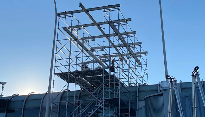 Systems scaffold on a rooftop with horizontal steel beams against a clear blue sky